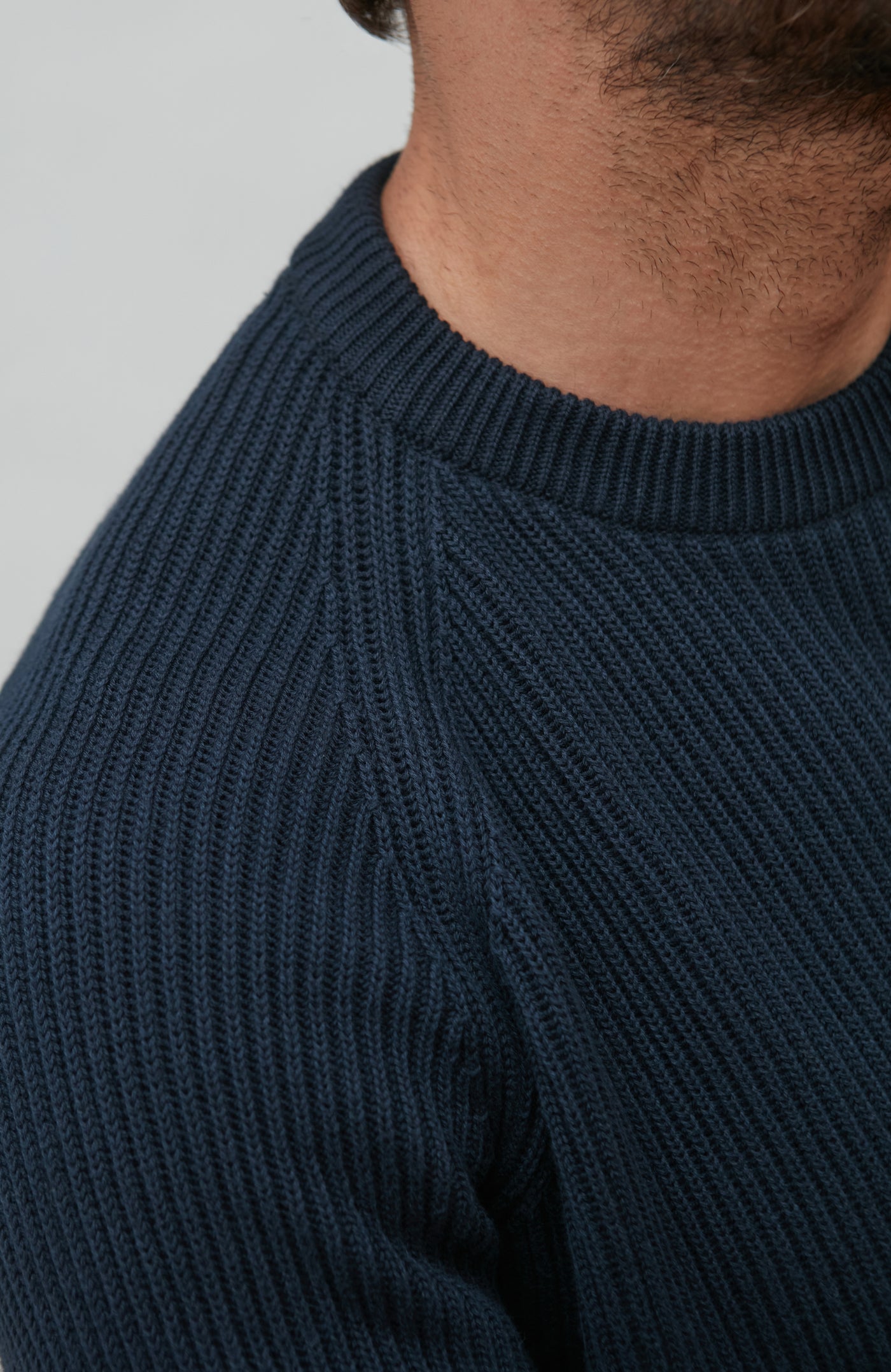 Close-up of a person wearing a dark blue rib fisherman sweater with a plain background