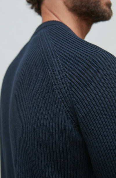 Close-up of a person wearing a dark blue ribbed sweater against a light gray background