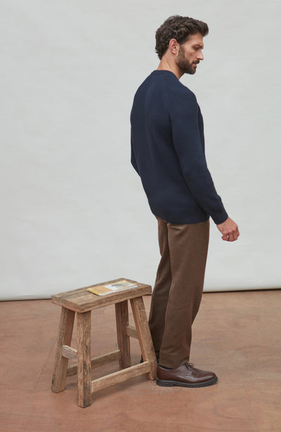 Man wearing a navy ribbed fisherman sweater and brown pants against a plain background