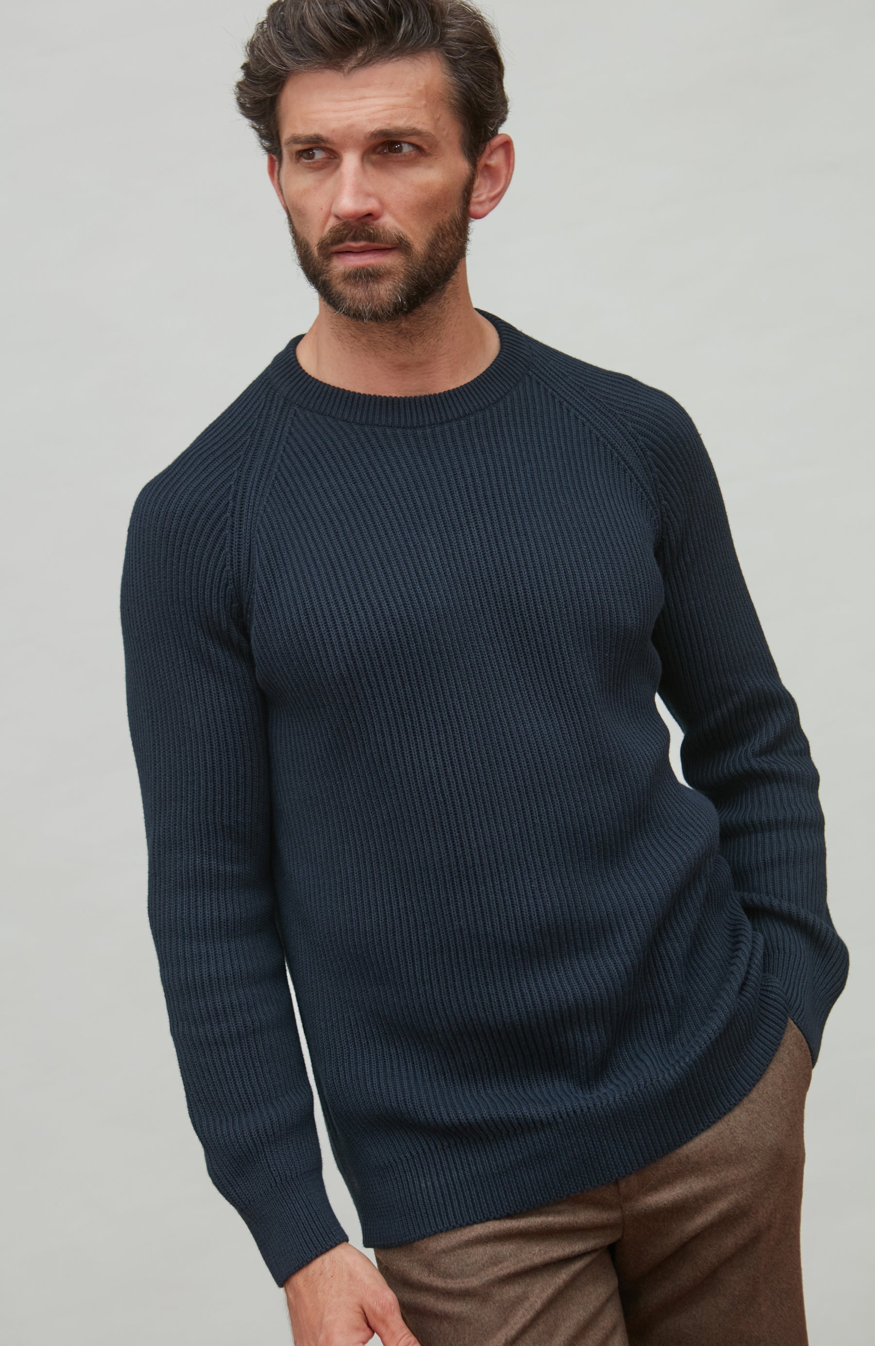 Man wearing a dark blue fisherman rib sweater against a plain background