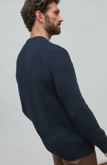 Man wearing a dark blue fisherman sweater against a light gray background