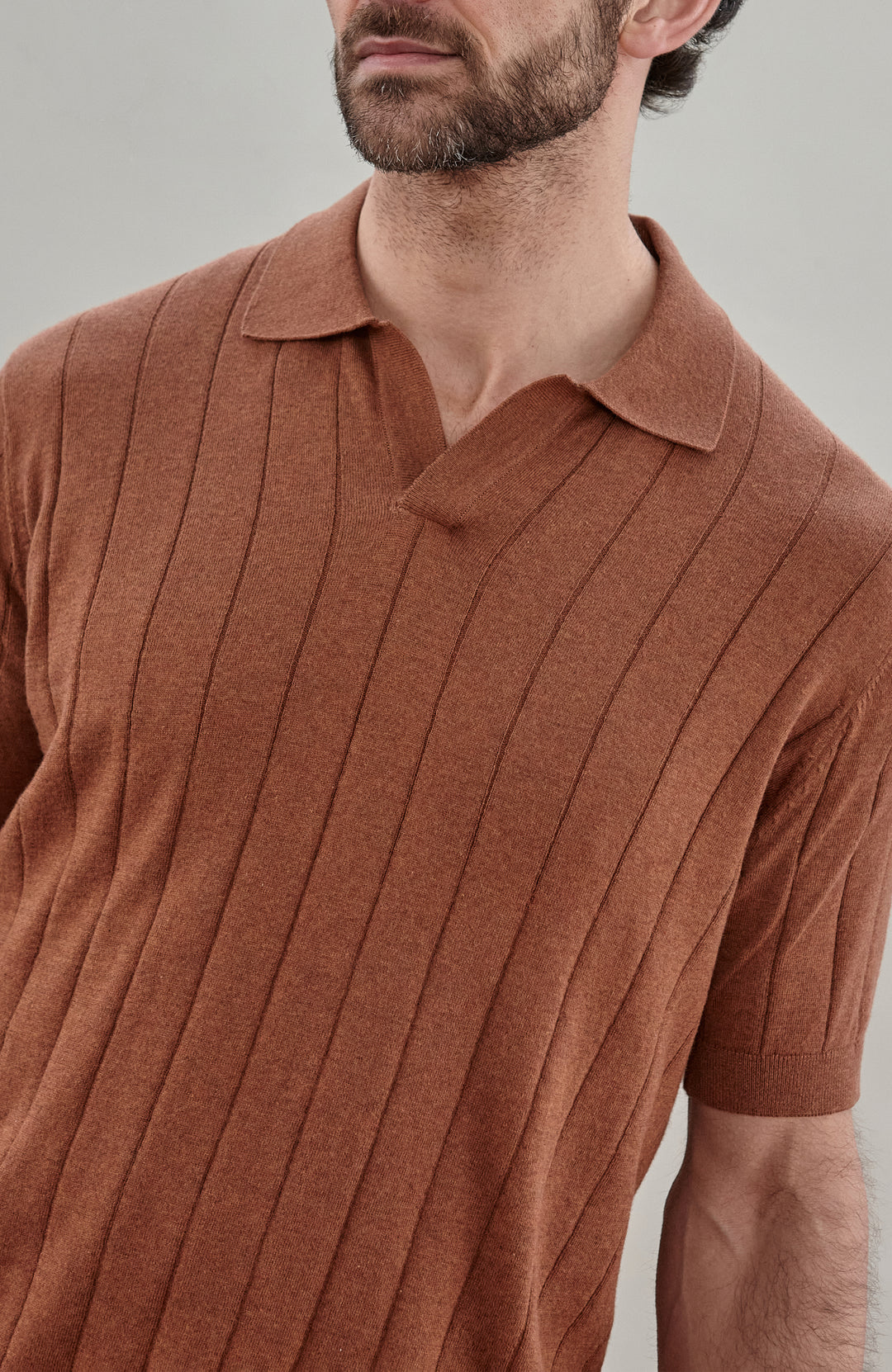 Man wearing a brown cotton ribbed polo shirt by Paul James Knitwear against a plain background