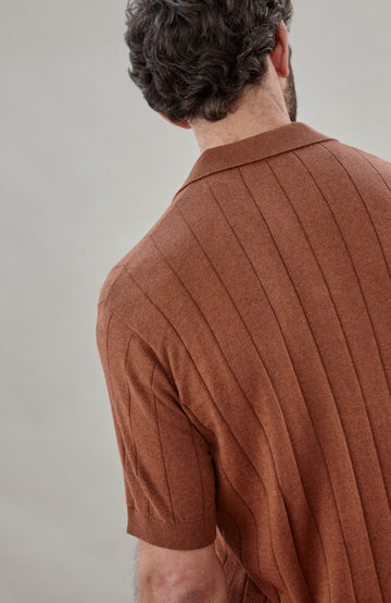 Man wearing a brown cotton ribbed polo shirt by Paul James Knitwear against a plain background