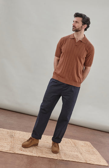 Man wearing a brown cotton ribbed polo shirt by Paul James Knitwear against a plain background