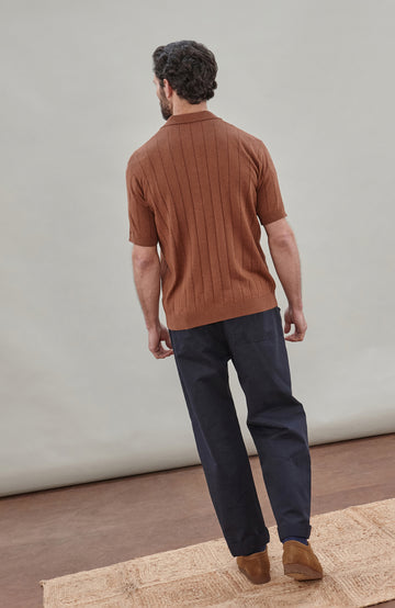 Man wearing a brown cotton ribbed polo shirt by Paul James Knitwear against a plain background