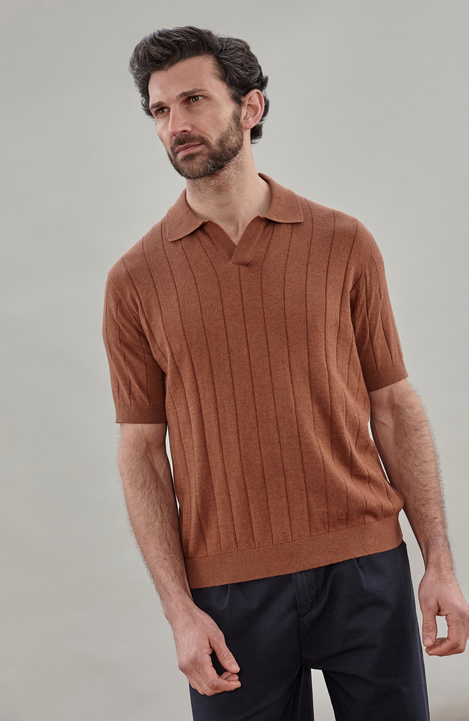 Man wearing a brown cotton ribbed polo shirt by Paul James Knitwear against a plain background