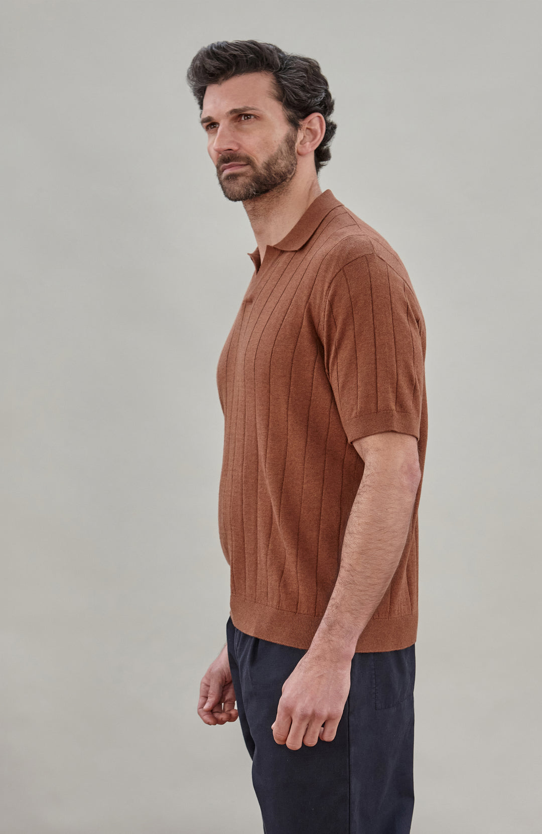 Man wearing a brown cotton ribbed polo shirt by Paul James Knitwear against a plain background