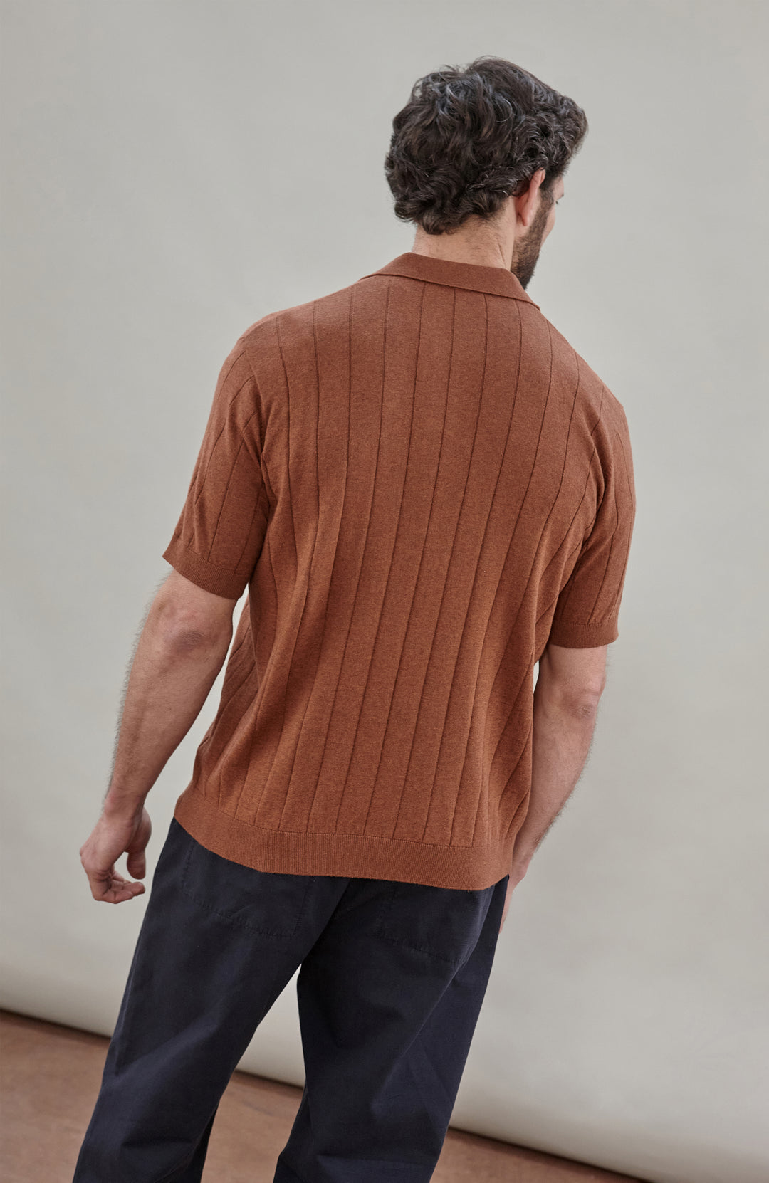 Man wearing a brown cotton ribbed polo shirt by Paul James Knitwear against a plain background
