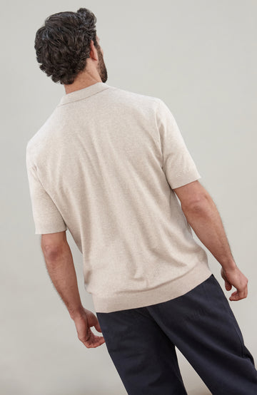 A man in profile wearing a light beige cotton knit short-sleeve polo shirt by Paul James Knitwear photographed against a neutral light gray studio background.