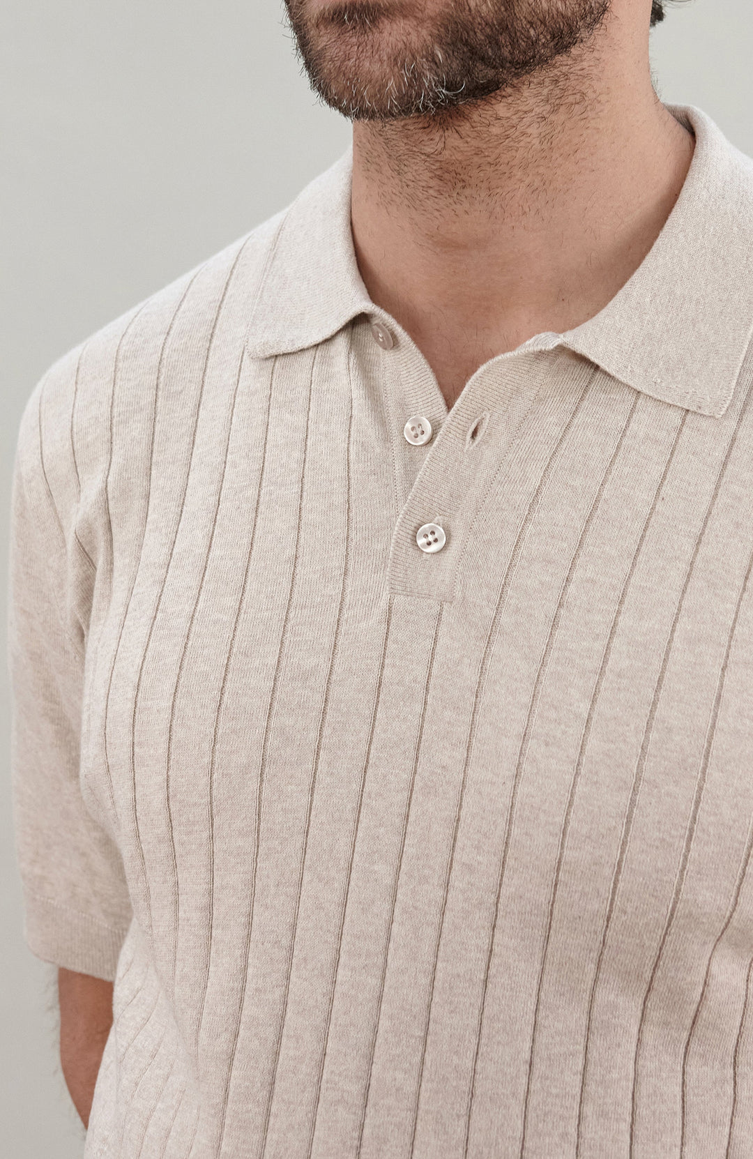 A man wearing a cream short-sleeve rib-knit cotton polo shirt by Paul James Knitwear, photographed against a neutral light gray background.
