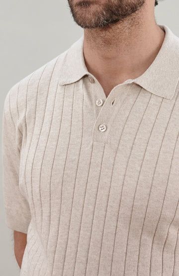 A man wearing a cream short-sleeve rib-knit cotton polo shirt by Paul James Knitwear, photographed against a neutral light gray background.