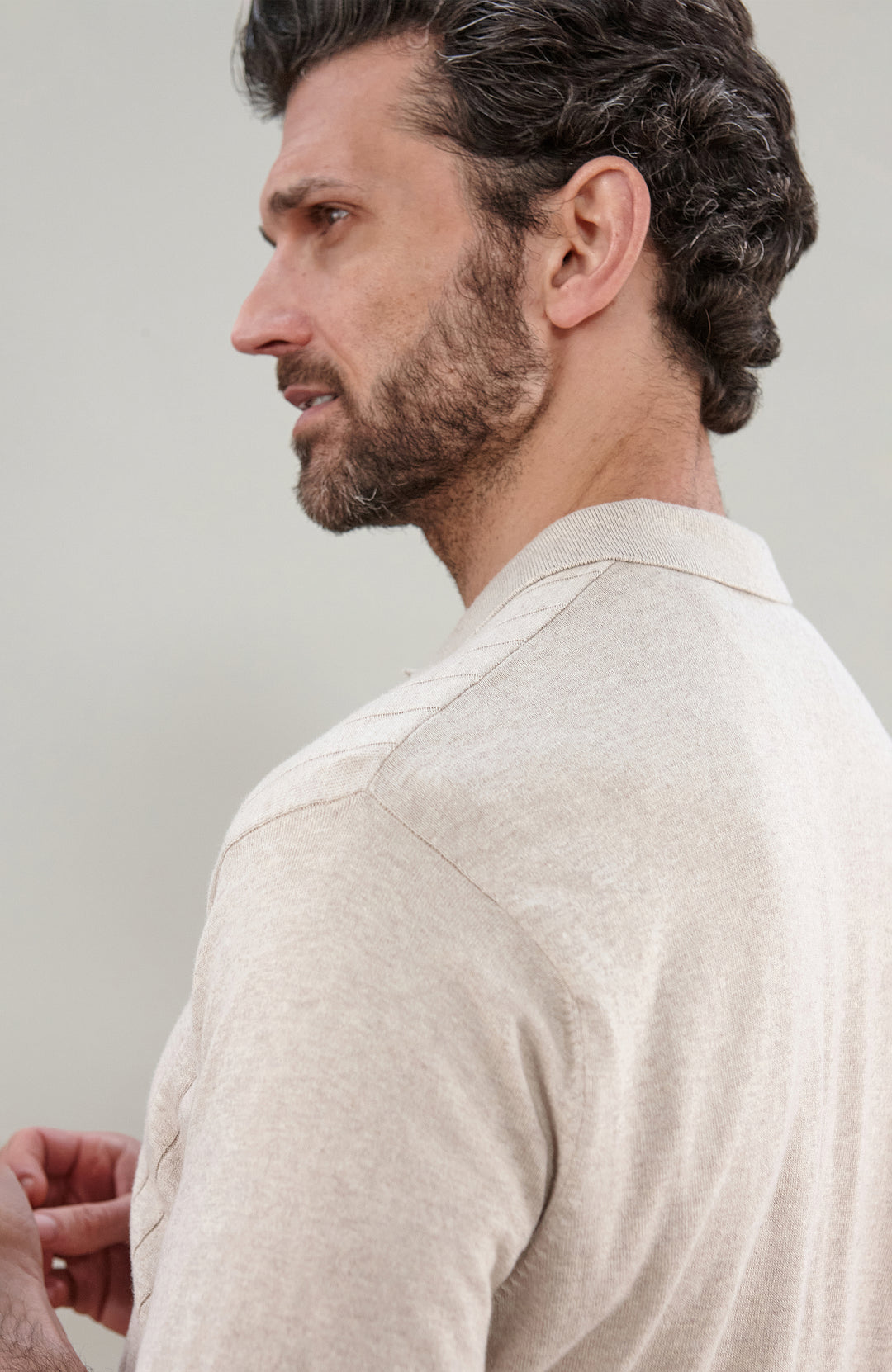 A man in profile wearing a light beige cotton knit short-sleeve polo shirt by Paul James Knitwear, shown from the chest up against a plain light gray background.