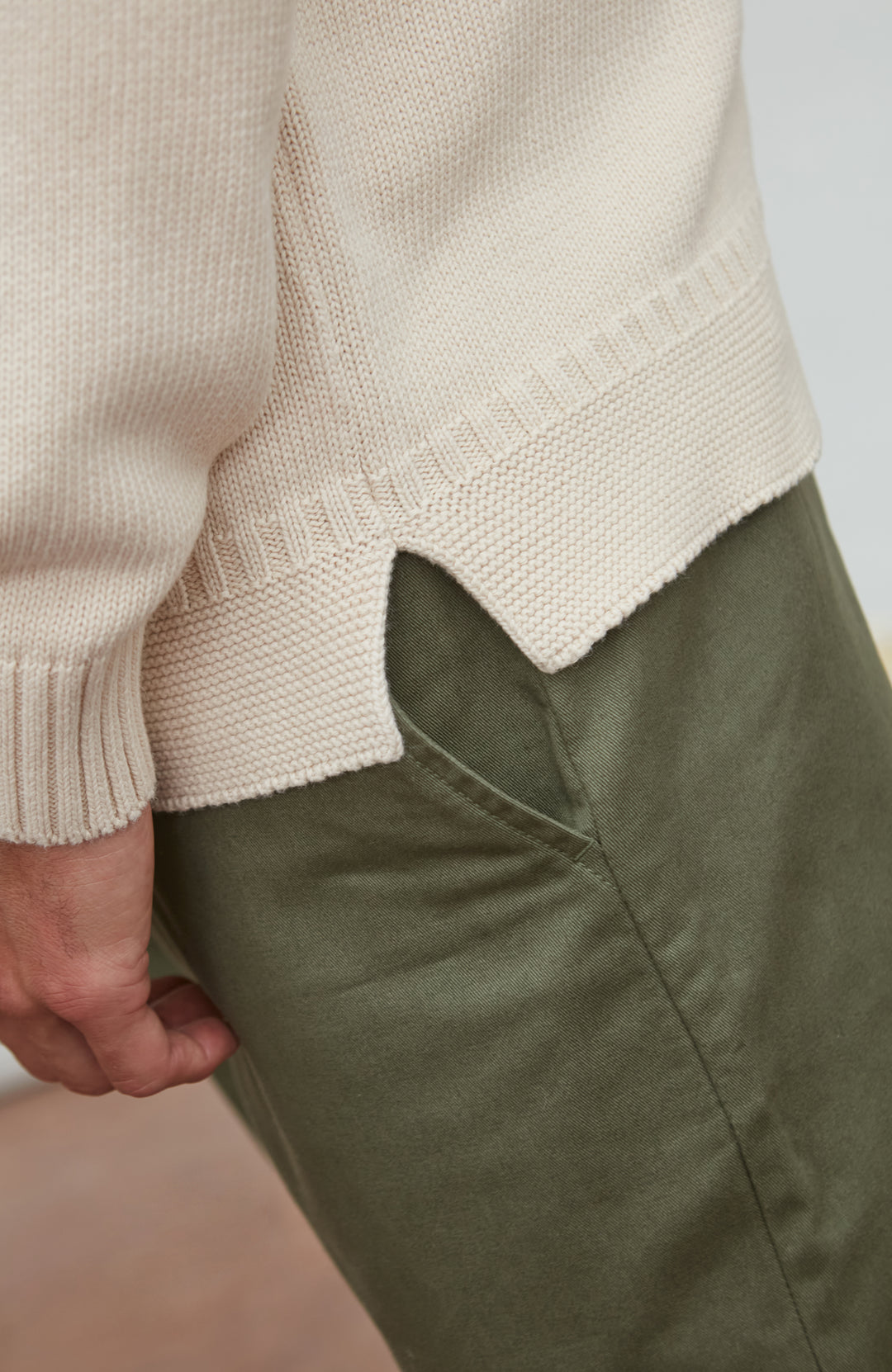 Close-up of a person wearing a guernsey sweater and green pants on a plain background