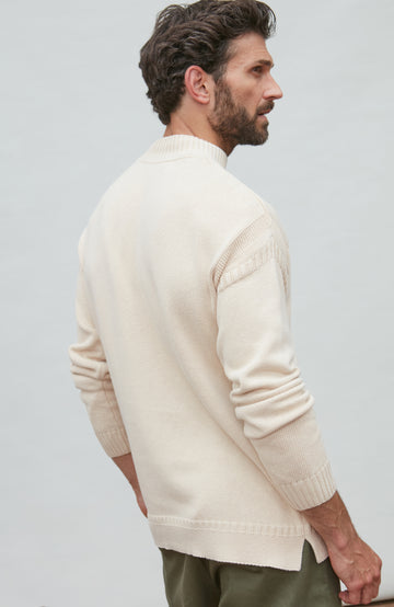 Man wearing a cream guernsey sweater against a light gray background