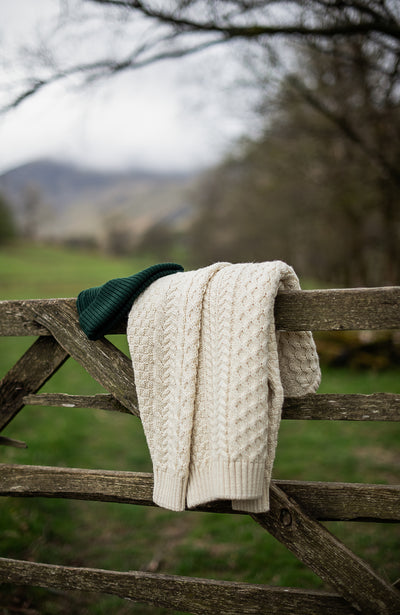 Knitted wool cable sweater hanging on a wooden fence with a scenic background