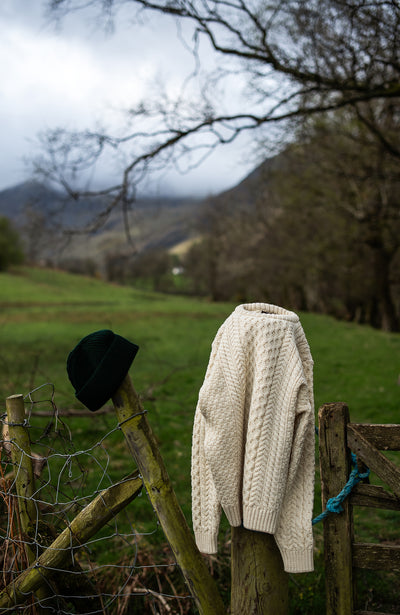 White knitted british wool sweater and black hat hanging on a wooden fence with a scenic background