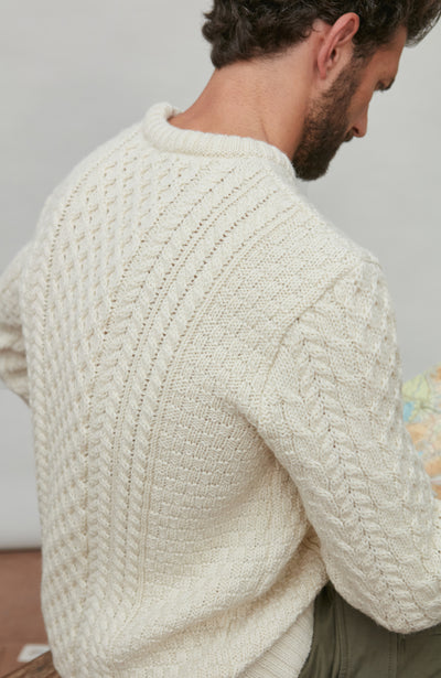 Man wearing a cream cable wool knitted sweater against a plain background
