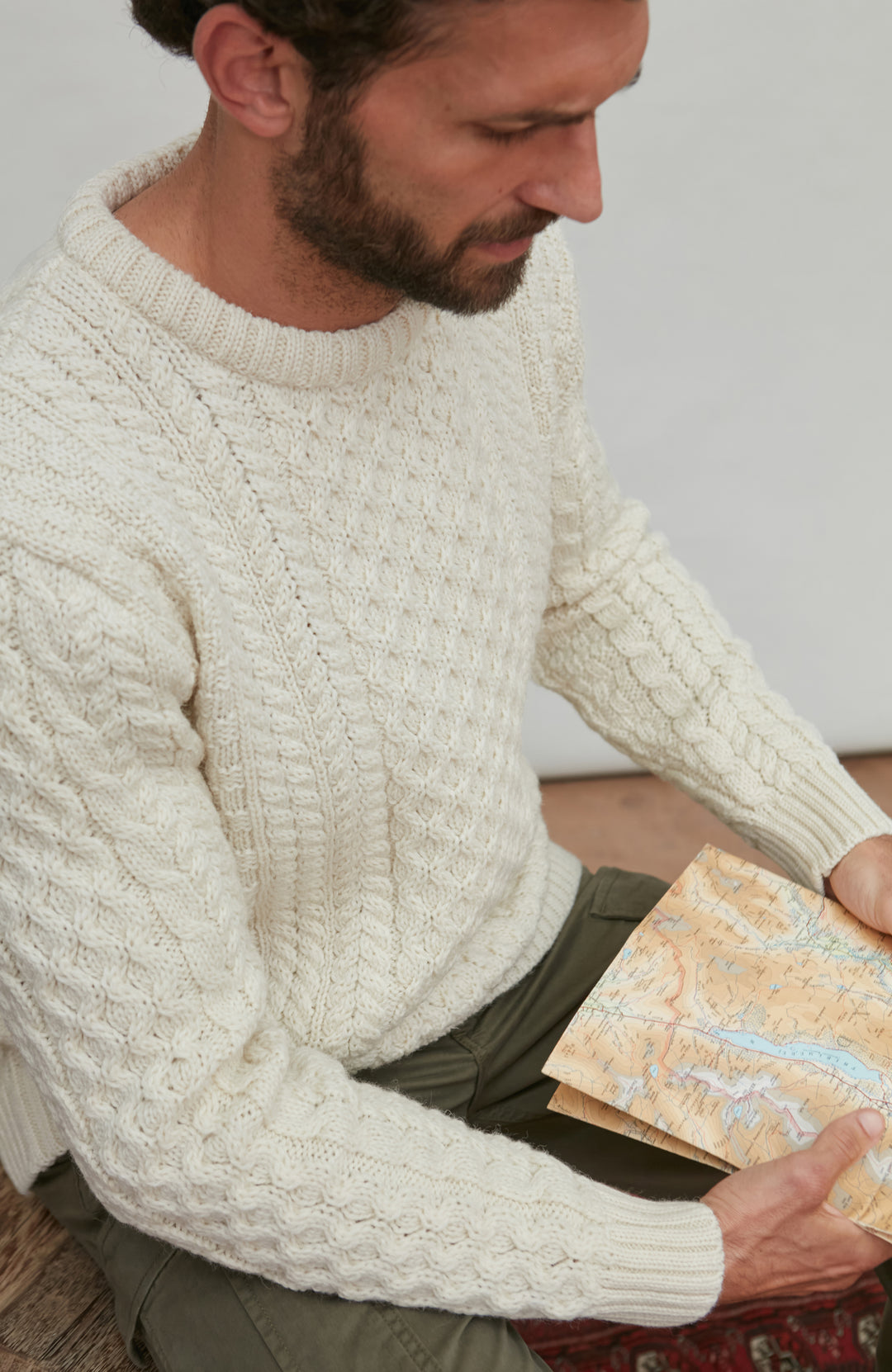 Man wearing a cream British wool sweater holding a pattern book By Paul James