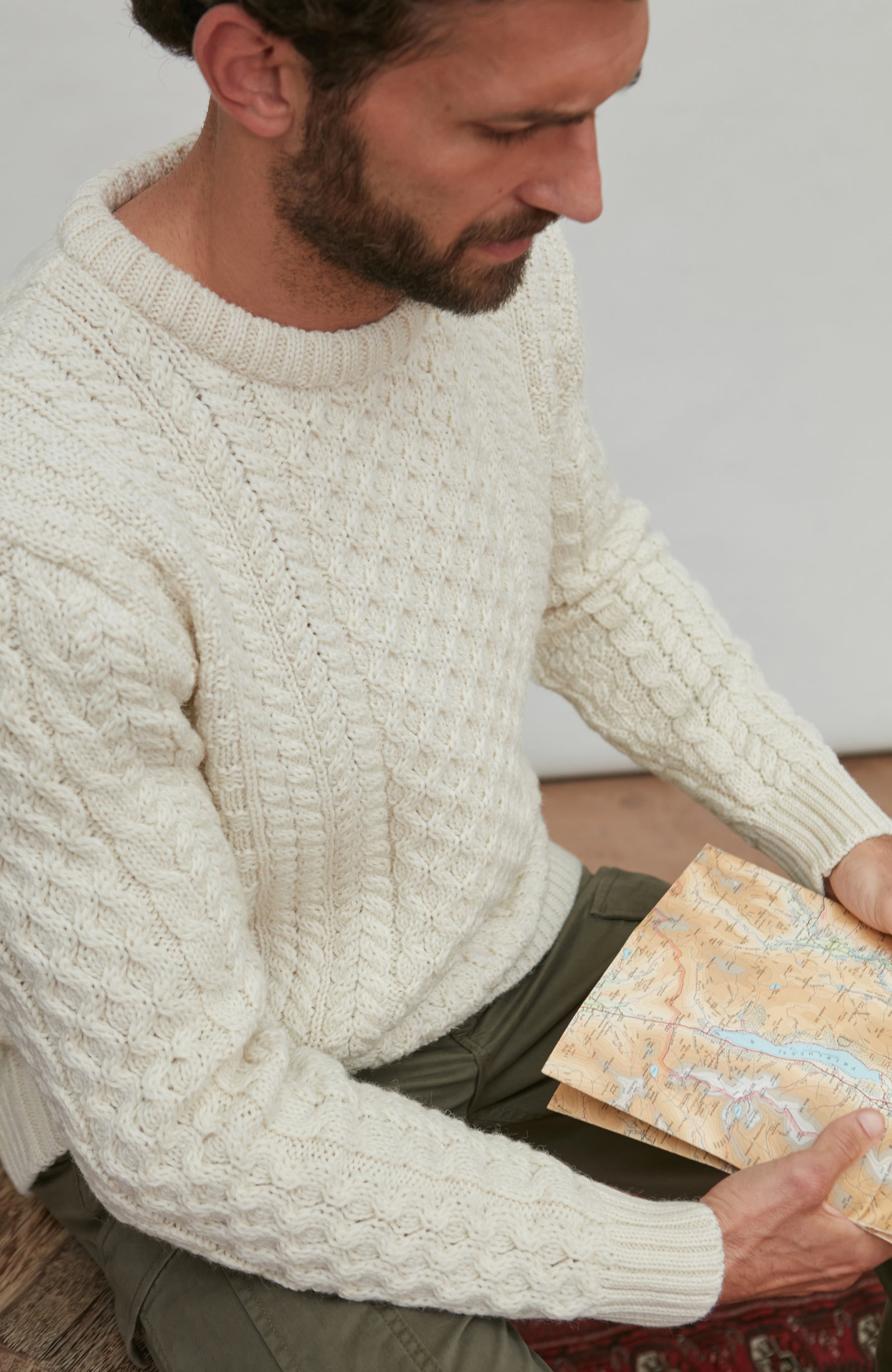Man wearing a cream British wool sweater holding a pattern book By Paul James