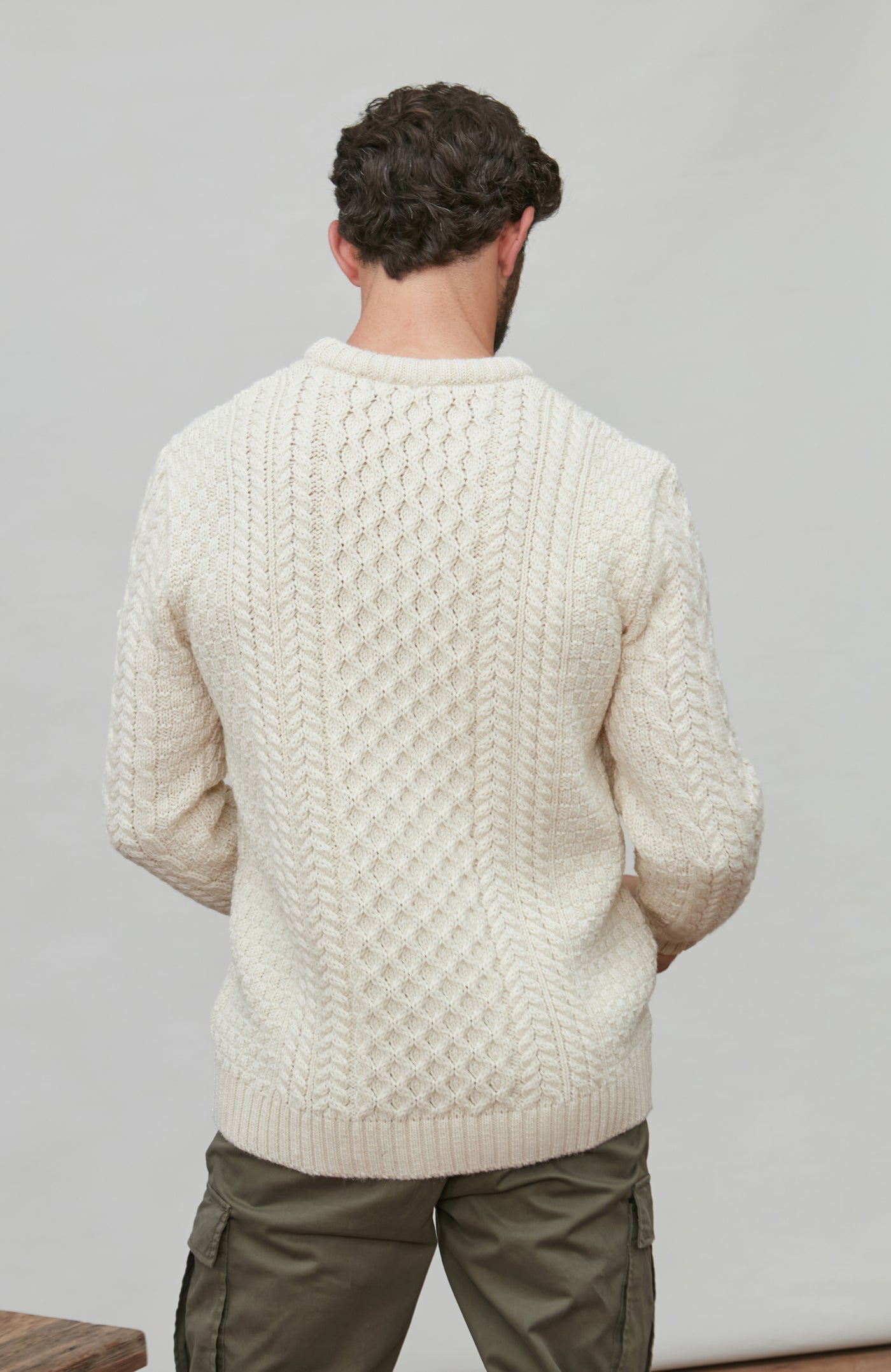 Man wearing a cream knitted wool sweater against a plain background