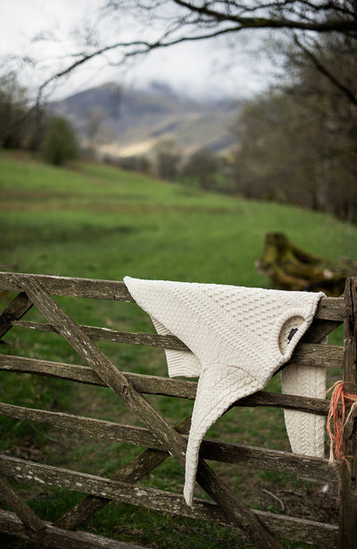 Knitted wool jumper on a wooden fence with a scenic background of green fields and mountains.