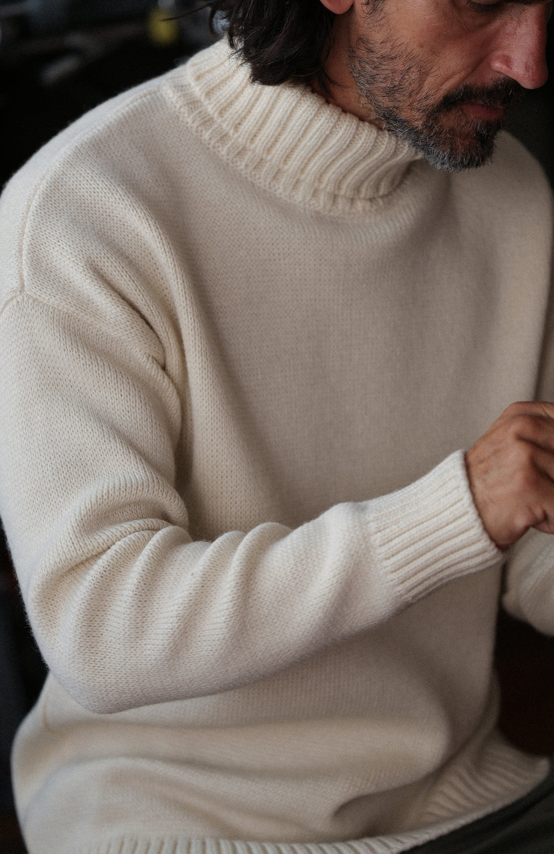 A man wearing a cream-colored merino wool submariner jumper by Paul James Knitwear made in England turtleneck sweater