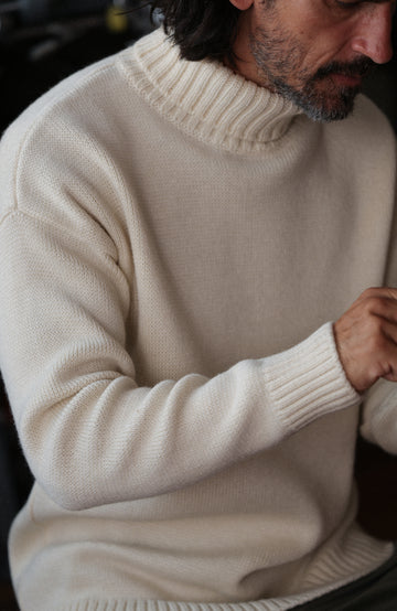 A man wearing a cream-colored merino wool submariner jumper by Paul James Knitwear made in England turtleneck sweater