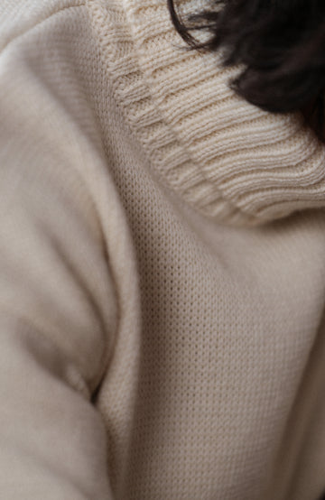 A man wearing a cream-colored merino wool submariner jumper by Paul James Knitwear made in England turtleneck sweater