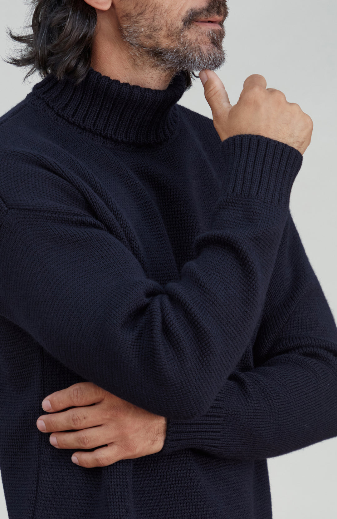 A close-up of a man wearing a dark navy blue ribbed knit turtleneck sweater, showing the texture of the fabric and the collar detail. Made by Paul James Knitwear.  Submariner sweater