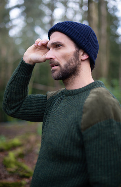 Man wearing a dark green sweater and wool fisherman beanie in a forest setting