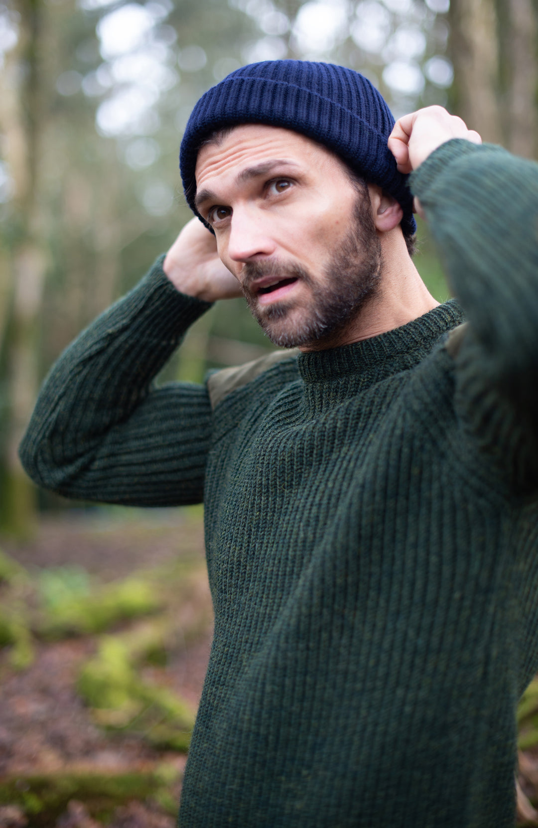 Man wearing a green sweater and navy wool beanie in a forest setting by paul james knitwear