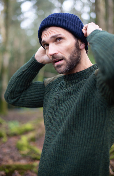 Man wearing a green sweater and navy wool beanie in a forest setting by paul james knitwear