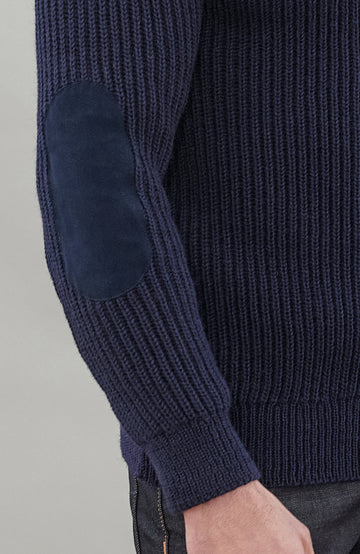 Man wearing a navy blue British wool made in England ribbed shooting sweater against a plain background