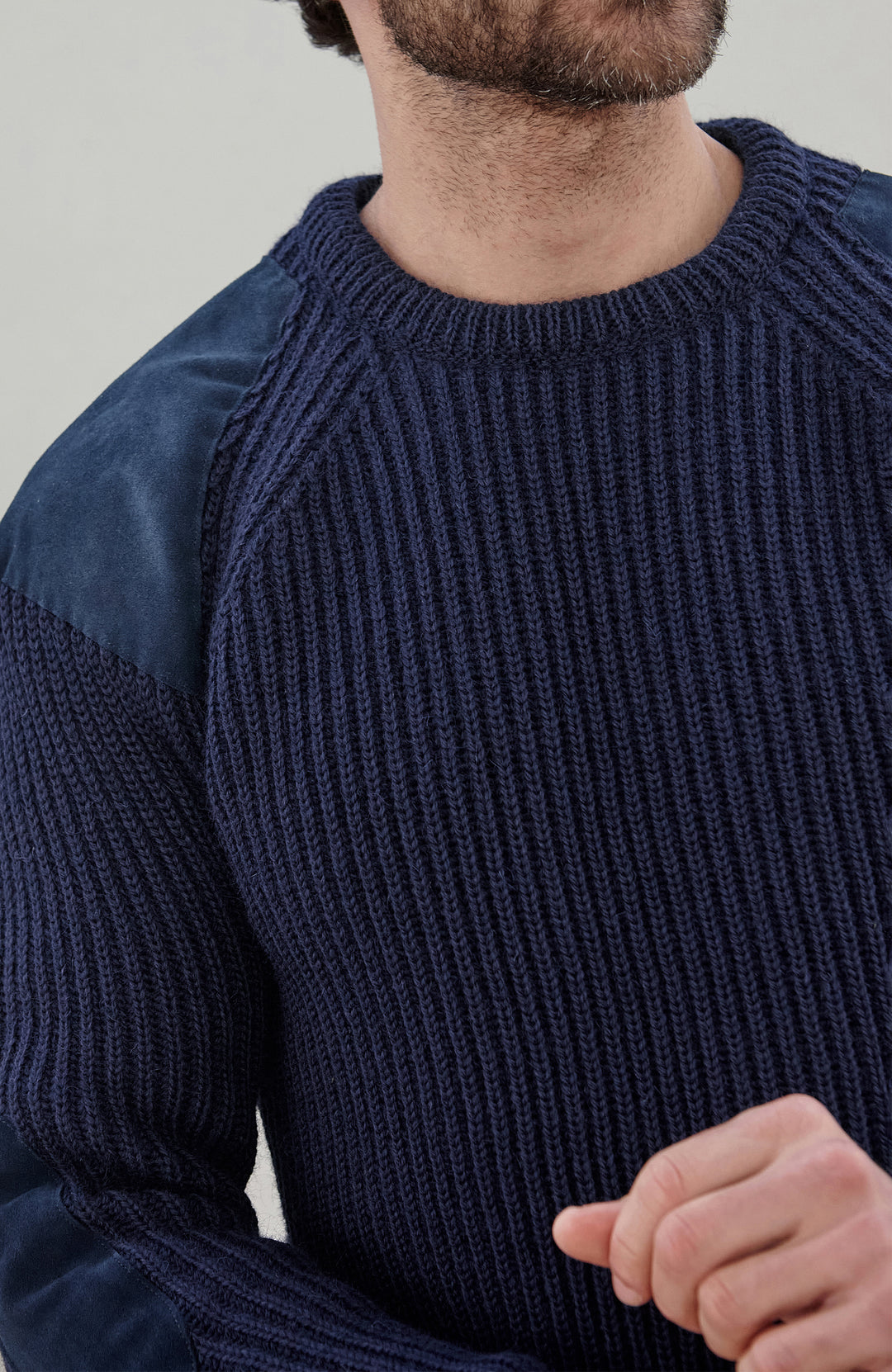 Close-up of a man wearing a navy blue ribbed knit sweater with contrasting dark blue velvet shoulder panels.