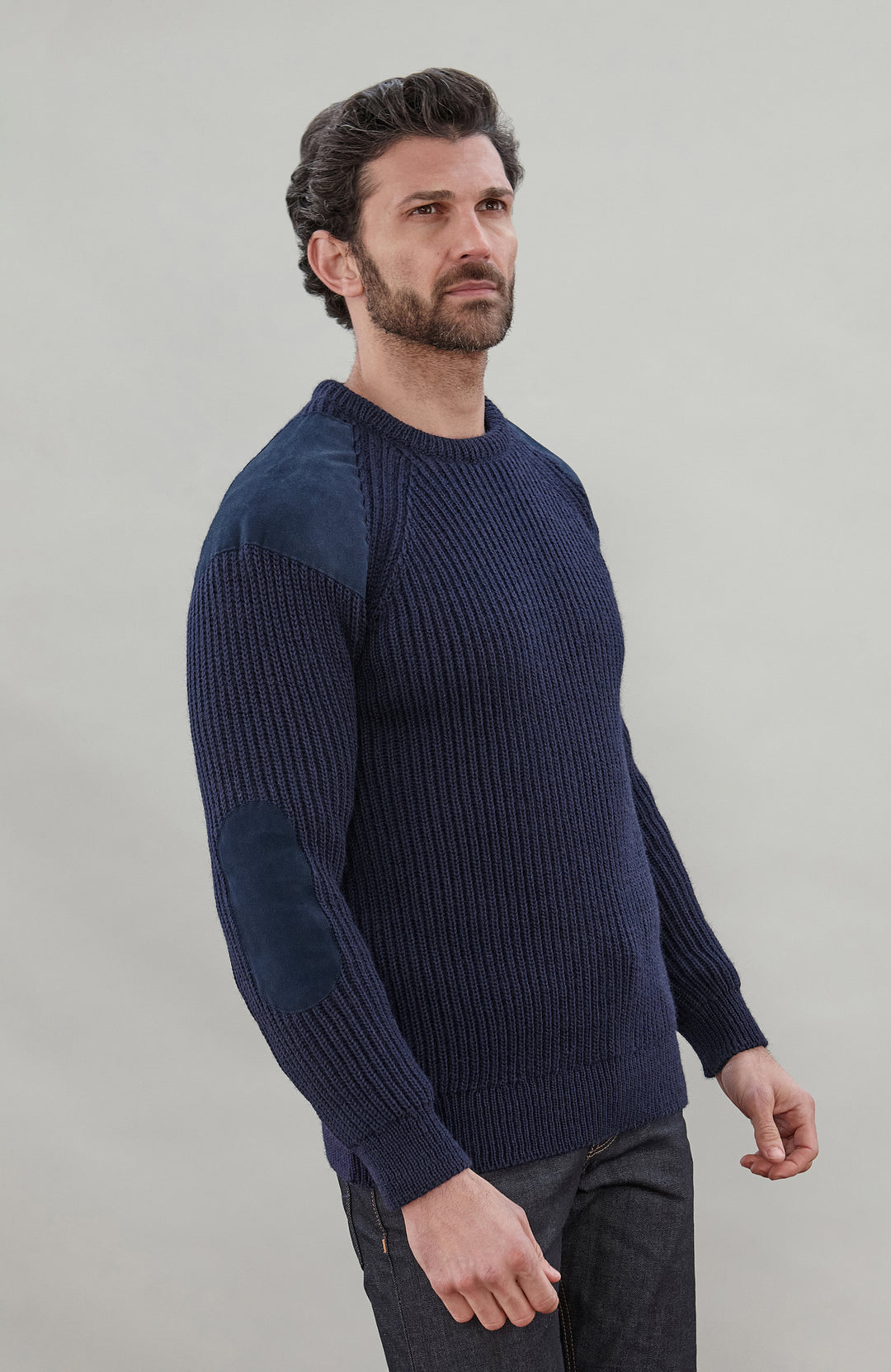 Man wearing a navy blue British wool made in England ribbed shooting sweater against a plain background