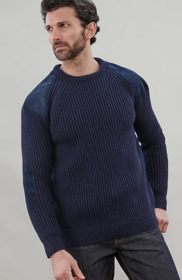 Man wearing a navy blue British wool made in England ribbed shooting sweater against a plain background