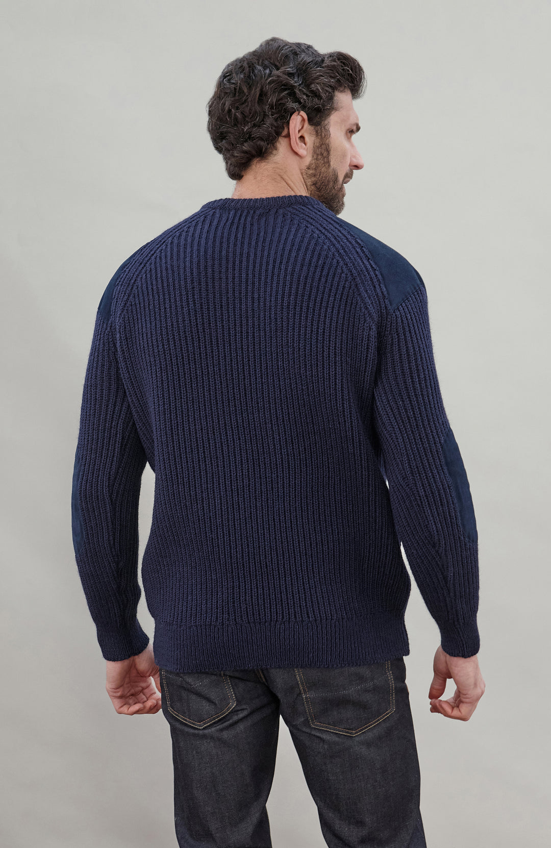 Man wearing a navy blue British wool made in England ribbed shooting sweater against a plain background