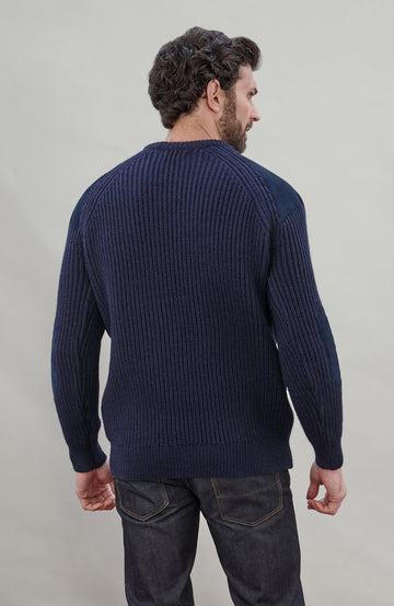 Man wearing a navy blue British wool made in England ribbed shooting sweater against a plain background