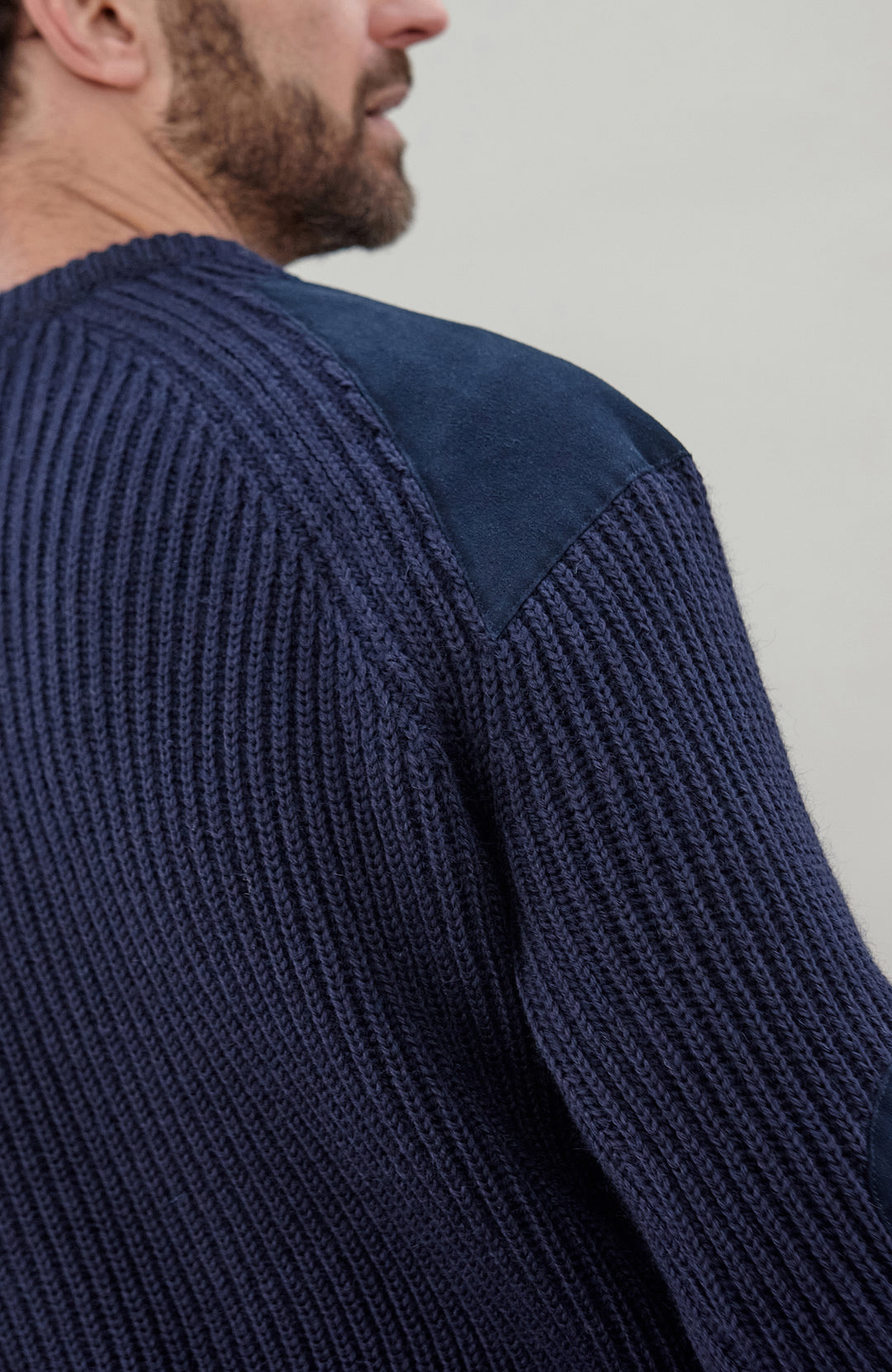 Man wearing a navy blue British wool made in England ribbed shooting sweater against a plain background