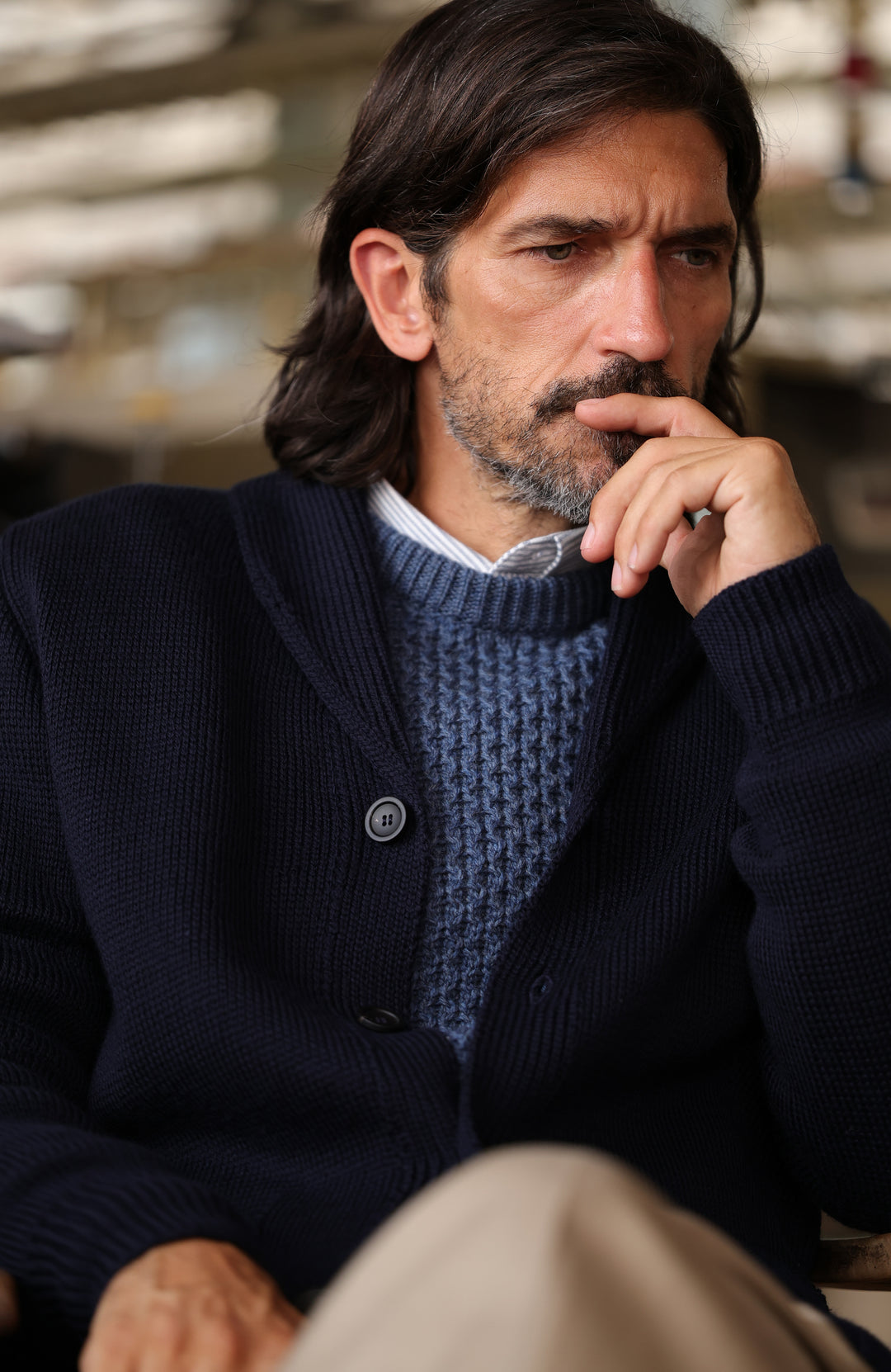A man wearing a dark navy made in england merino wool navy shawl collar cardigan by Paul James Knitwear over a textured blue knit wool fisherman sweater