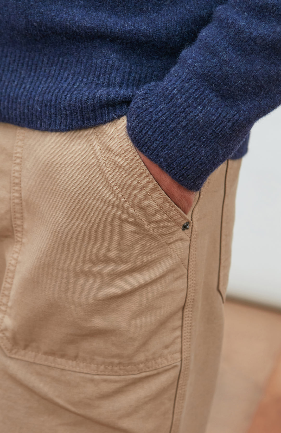 A man wearing a navy blue knit mock neck wool sweater by paul james knitwear made in england and khaki pants, photographed against a light gray studio background.