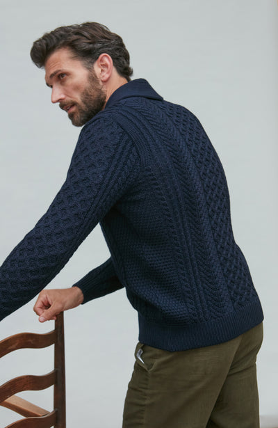 Man wearing a navy wool cable knit cardigan sitting on a wooden chair.