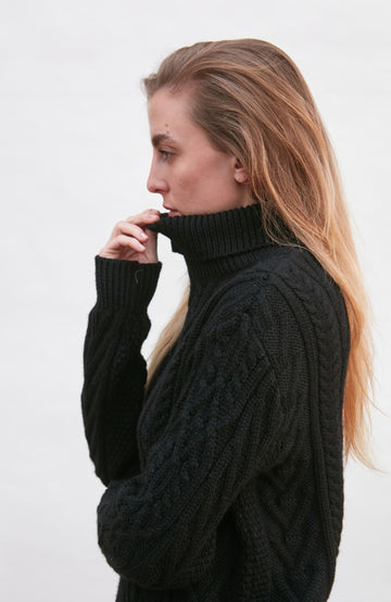 Woman wearing a black cable knit sweater by paul james knitwear