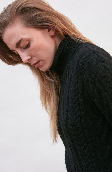 Woman wearing a black cable knit wool sweater by paul james knitwear