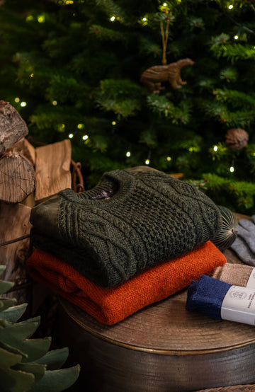 Stack of green and orange sweaters with a Christmas tree in the background