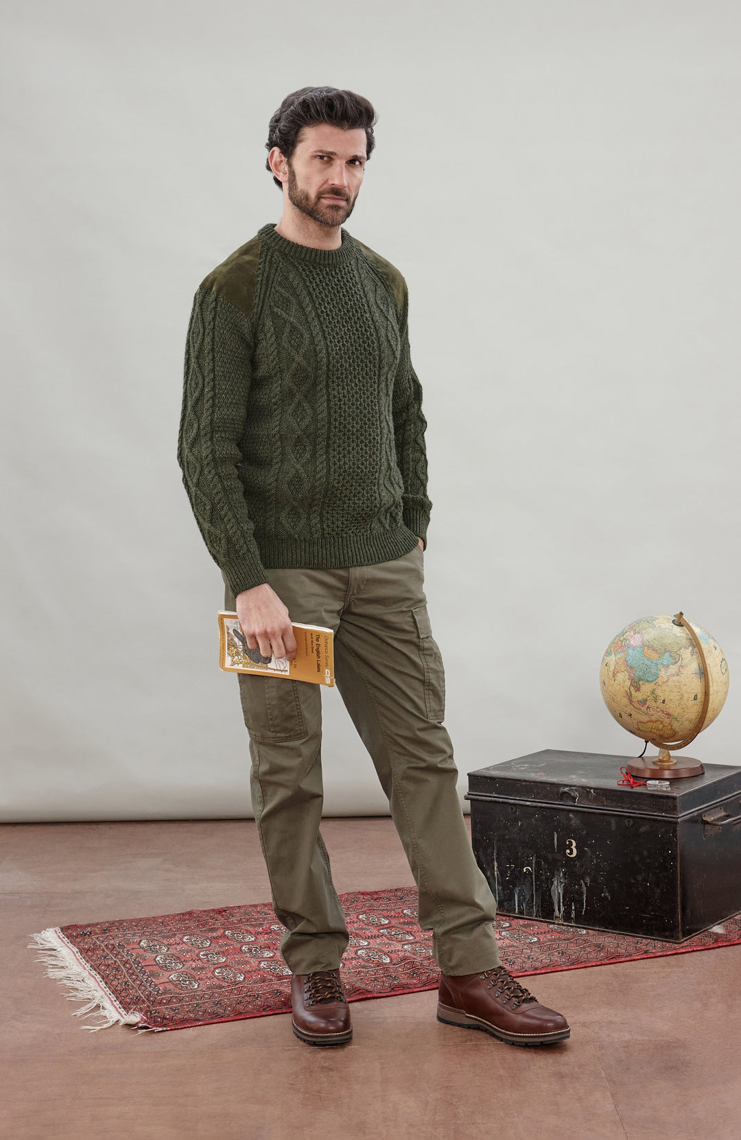 A man wearing a dark olive green cable-knit made in England sweater by Paul James Knitwear