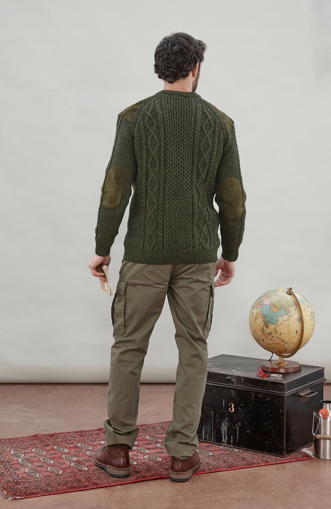 A man wearing a dark olive green cable-knit made in England sweater by Paul James Knitwear