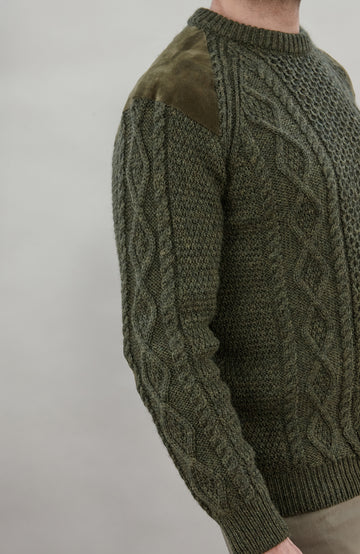 A man wearing a dark olive green cable-knit made in England sweater by Paul James Knitwear