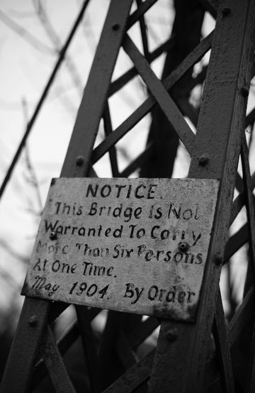 Black and white sign on a bridge structure with text about weight limits.