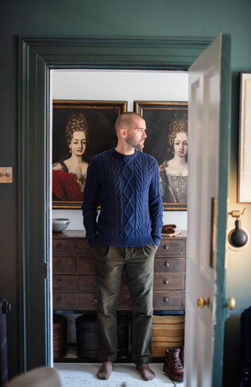 Man standing in a room with classical paintings on the wall by Paul James